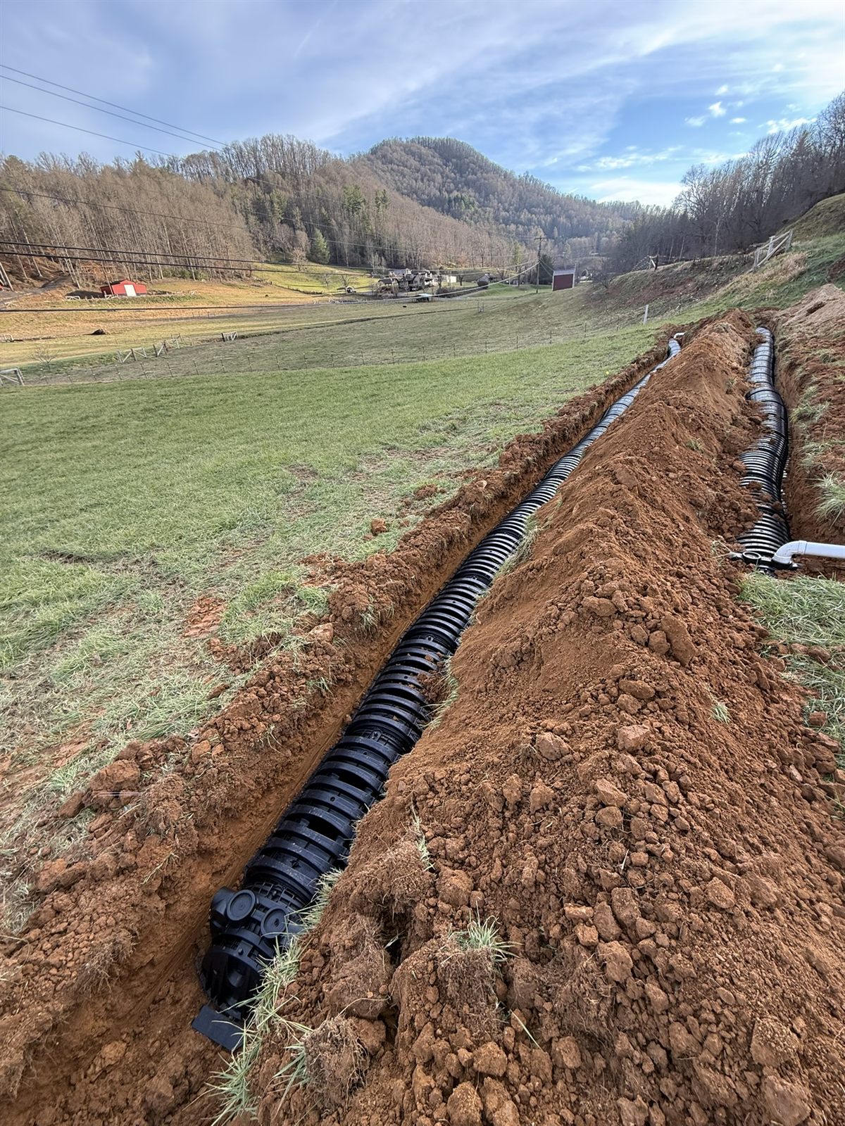 Long curtain drain trench with pipe and gravel run across a pasture, Western NC