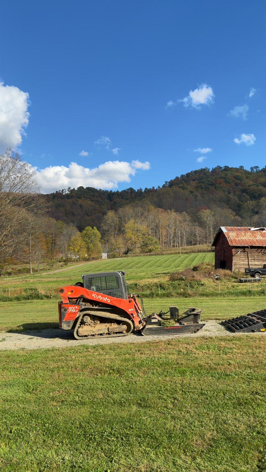 Compact track loader on a mountain pasture with a barn in Western NC