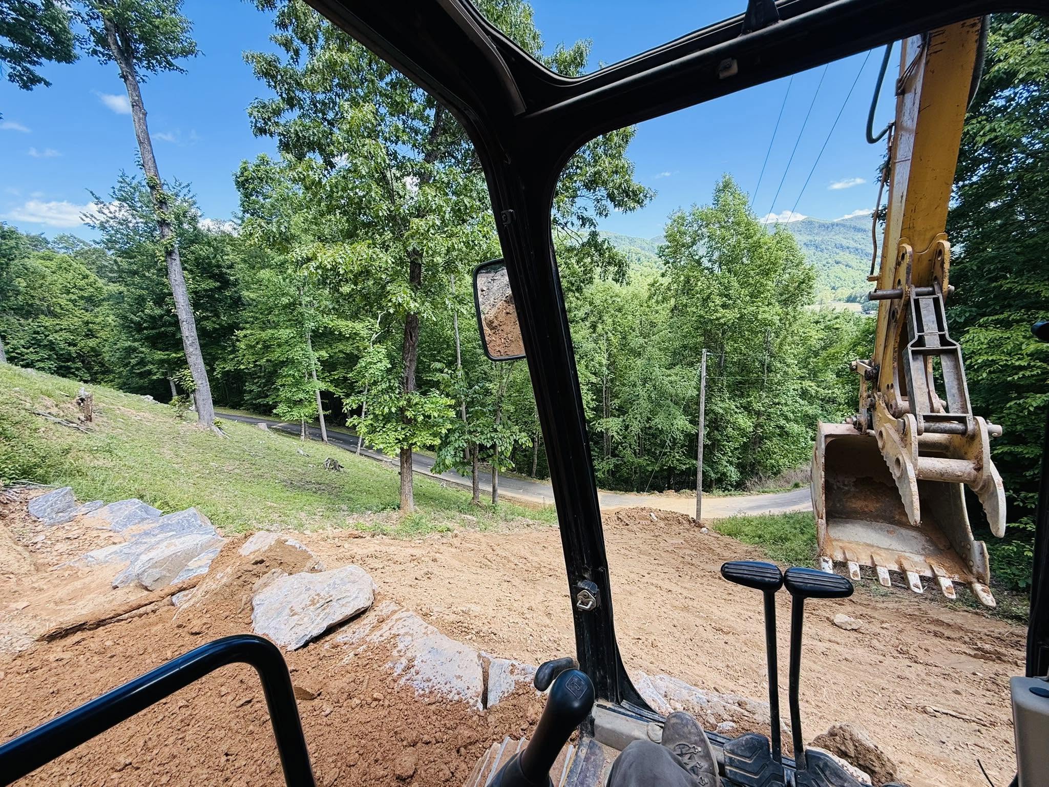 View from the excavator cab placing boulders and grading a steep rocky mountain lot in Western NC