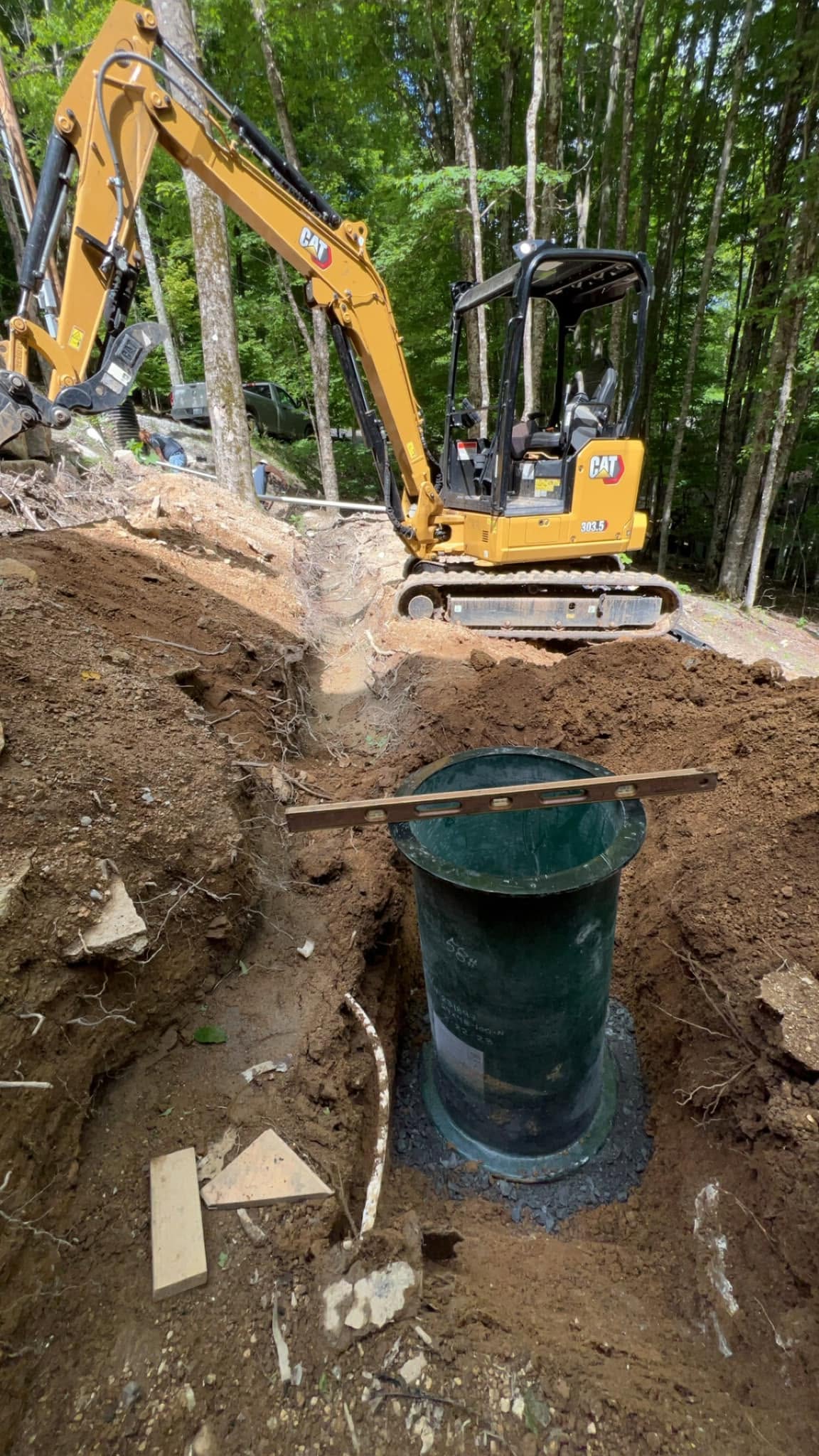 Compact excavator setting a septic pump basin in an excavation on a residential site near Burnsville, NC